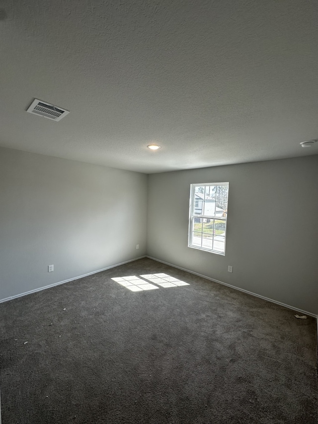 spare room featuring visible vents, dark carpet, a textured ceiling, and baseboards