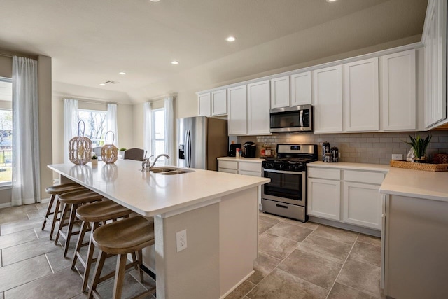 kitchen with sink, a kitchen breakfast bar, stainless steel appliances, an island with sink, and white cabinets