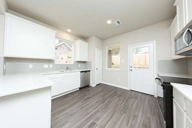 kitchen with stainless steel appliances, light wood finished floors, a sink, and white cabinetry