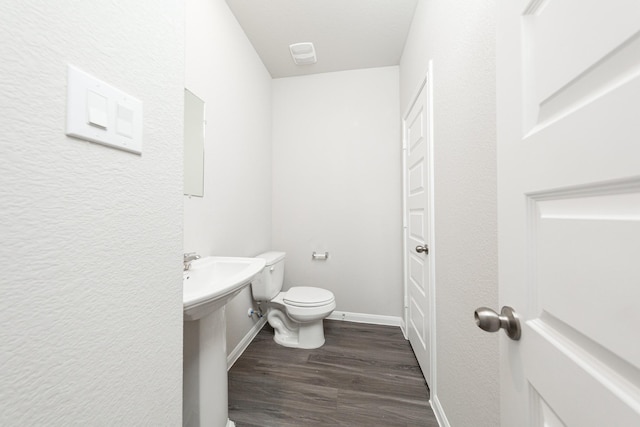 half bath with a sink, wood finished floors, toilet, and baseboards