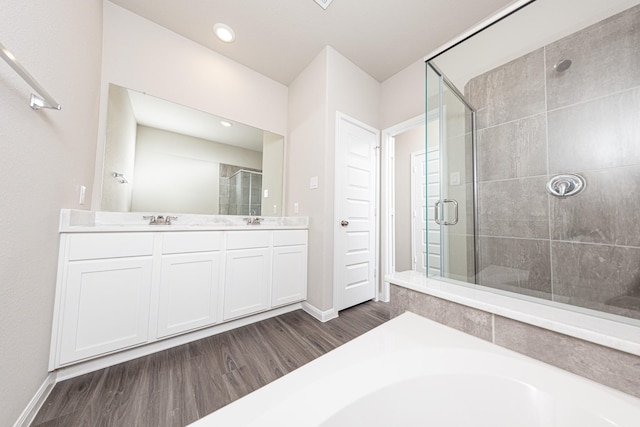 bathroom featuring double vanity, a shower stall, a sink, and wood finished floors