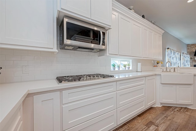 kitchen featuring sink, light hardwood / wood-style flooring, backsplash, stainless steel appliances, and white cabinets