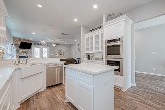 kitchen featuring white cabinetry, hanging light fixtures, a center island, light hardwood / wood-style floors, and stainless steel appliances