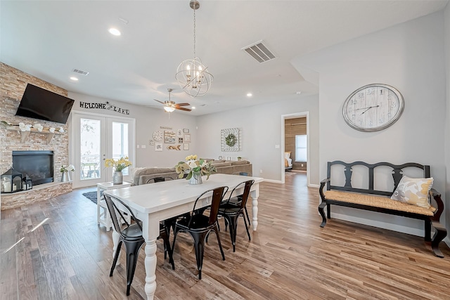 dining room featuring a fireplace, ceiling fan with notable chandelier, and light hardwood / wood-style flooring