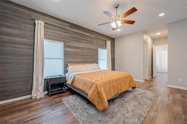 bedroom featuring hardwood / wood-style flooring, ceiling fan, and wood walls