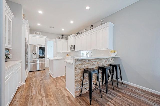 kitchen with white cabinetry, stainless steel appliances, a kitchen breakfast bar, a kitchen island, and kitchen peninsula