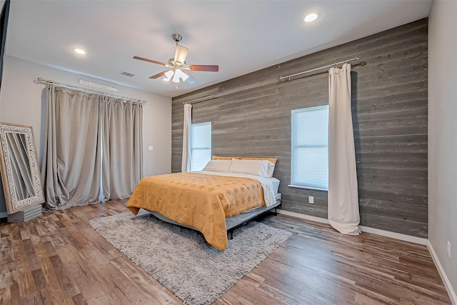 bedroom featuring wood-type flooring, wooden walls, and ceiling fan