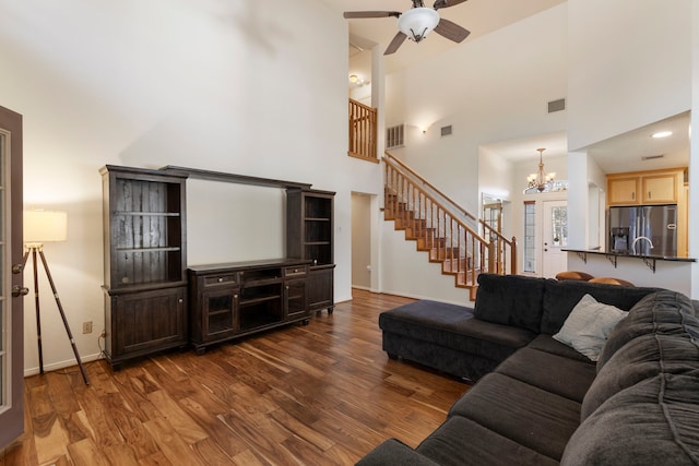 living room featuring dark wood-type flooring, a towering ceiling, and ceiling fan with notable chandelier