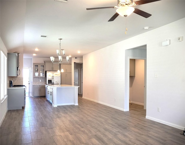 kitchen featuring a center island with sink, stainless steel refrigerator with ice dispenser, tasteful backsplash, light countertops, and hanging light fixtures