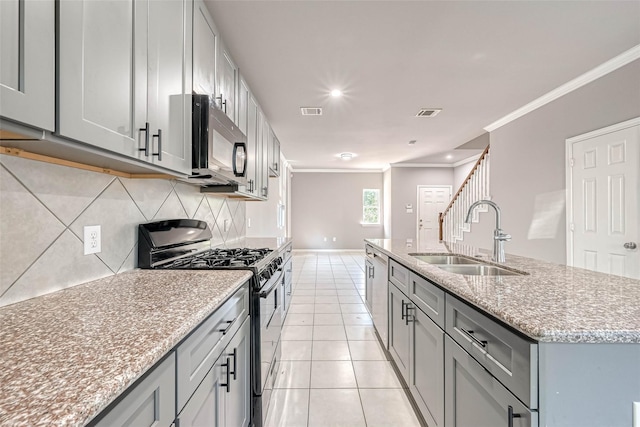 kitchen featuring light tile patterned flooring, an island with sink, sink, ornamental molding, and gas range