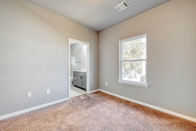 unfurnished bedroom featuring light colored carpet and ensuite bathroom