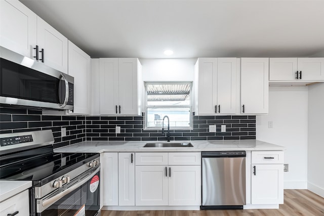 kitchen with white cabinetry, sink, light hardwood / wood-style floors, stainless steel appliances, and light stone countertops