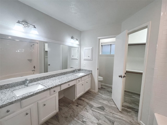 full bathroom featuring washtub / shower combination, vanity, wood-type flooring, a textured ceiling, and toilet