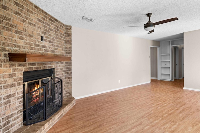 unfurnished living room featuring a brick fireplace, hardwood / wood-style floors, a textured ceiling, and ceiling fan