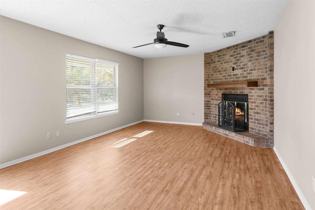 unfurnished living room with a brick fireplace, hardwood / wood-style flooring, a textured ceiling, and ceiling fan