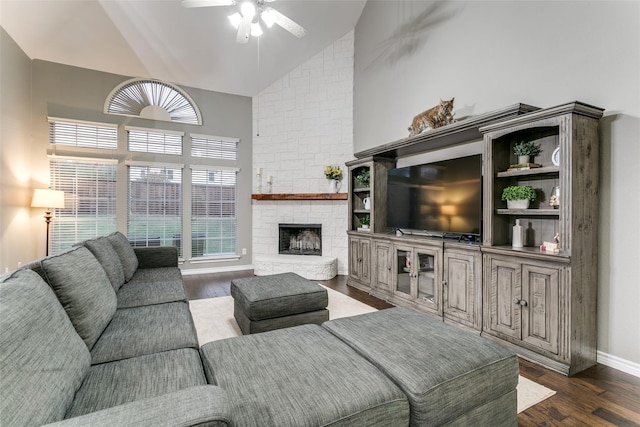 living room with dark wood-type flooring, ceiling fan, a stone fireplace, and high vaulted ceiling