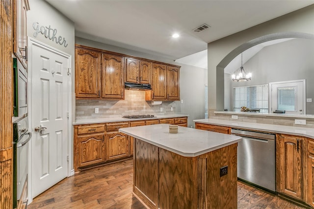 kitchen with pendant lighting, appliances with stainless steel finishes, a center island, tasteful backsplash, and dark hardwood / wood-style flooring