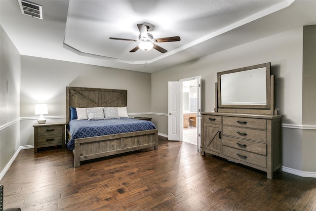 bedroom with ensuite bath, dark wood-type flooring, a raised ceiling, and ceiling fan