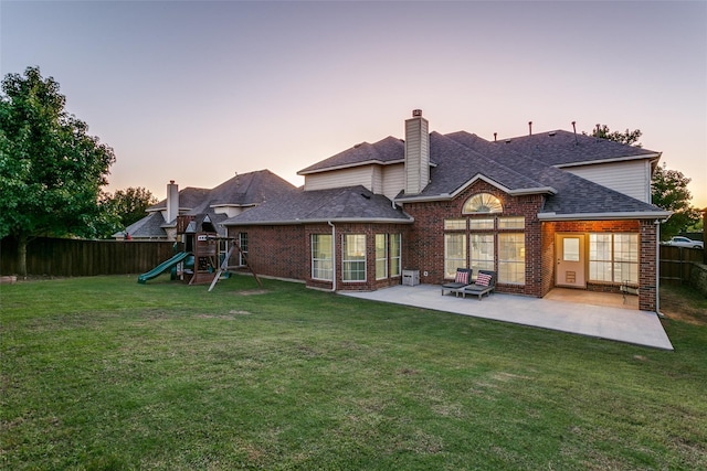 back house at dusk with a playground, a patio, and a lawn