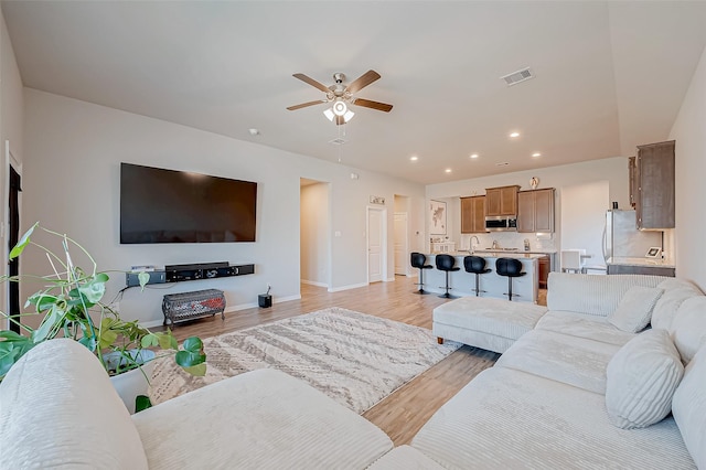 living room with ceiling fan, sink, and light wood-type flooring