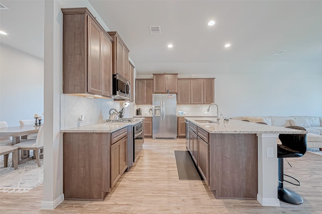 kitchen featuring a breakfast bar, sink, light hardwood / wood-style flooring, an island with sink, and stainless steel appliances