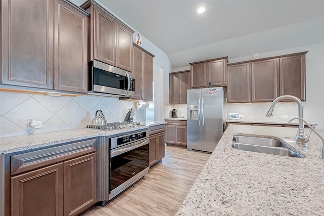 kitchen featuring sink, light stone counters, light wood-type flooring, appliances with stainless steel finishes, and backsplash