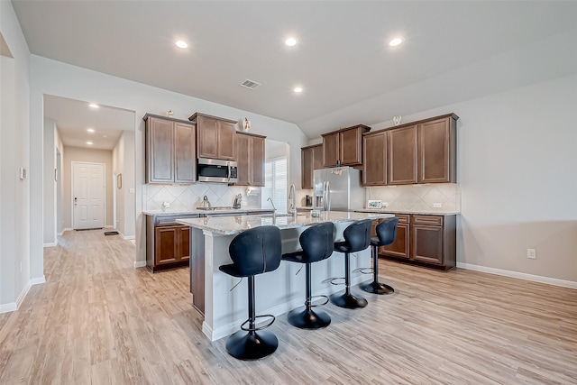 kitchen featuring a breakfast bar, light stone counters, a center island with sink, light wood-type flooring, and appliances with stainless steel finishes