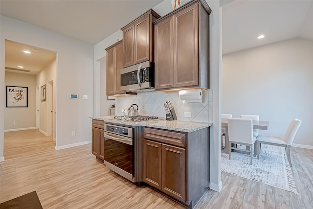 kitchen with light stone counters, stainless steel appliances, light hardwood / wood-style floors, and decorative backsplash