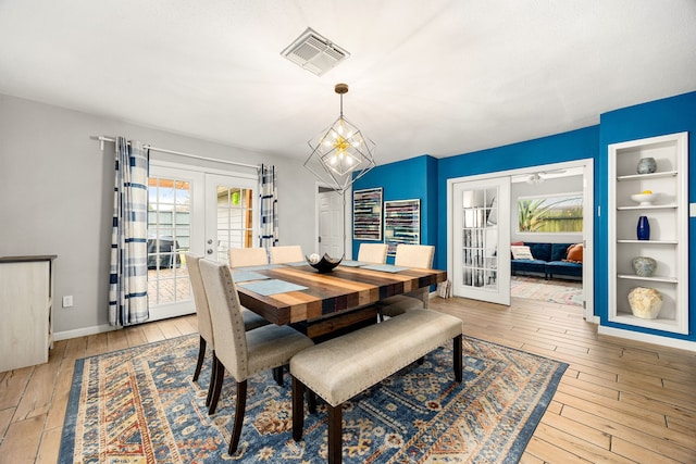 dining area with a notable chandelier, light hardwood / wood-style flooring, built in features, and french doors