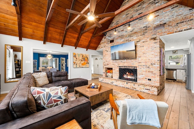 living room with light wood-type flooring, ceiling fan, wood ceiling, a brick fireplace, and beam ceiling