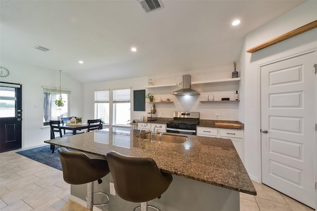 kitchen featuring sink, white cabinetry, ventilation hood, stainless steel range with gas cooktop, and a kitchen island with sink