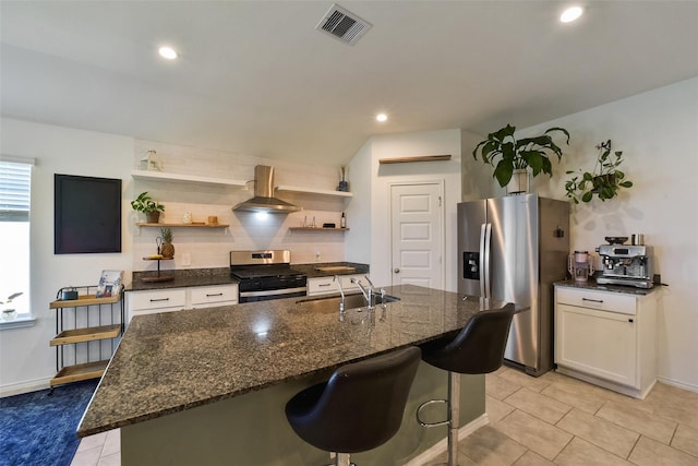 kitchen with wall chimney range hood, sink, appliances with stainless steel finishes, a kitchen island with sink, and white cabinets