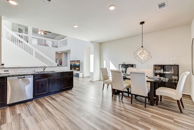 kitchen with sink, hanging light fixtures, light hardwood / wood-style floors, stainless steel dishwasher, and dark stone counters