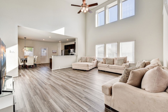 living room with ceiling fan, a towering ceiling, and light hardwood / wood-style flooring