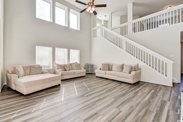 living room with hardwood / wood-style flooring, a towering ceiling, and ceiling fan