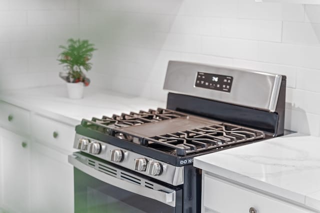 interior details featuring white cabinetry, light stone counters, and stainless steel gas range