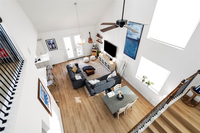 living room with high vaulted ceiling, a skylight, french doors, ceiling fan, and light hardwood / wood-style flooring