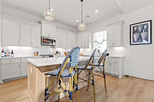 kitchen featuring decorative light fixtures, white cabinetry, a breakfast bar area, a center island, and light hardwood / wood-style flooring