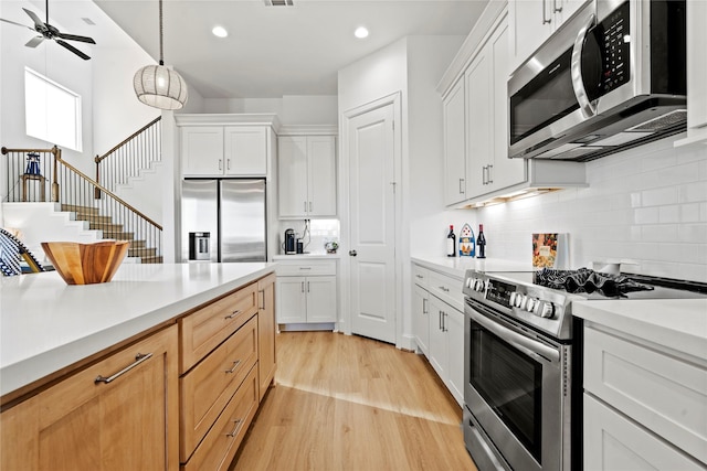 kitchen featuring white cabinetry, pendant lighting, light wood-type flooring, and appliances with stainless steel finishes