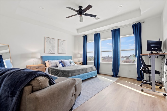 bedroom featuring light hardwood / wood-style flooring, ceiling fan, and a tray ceiling