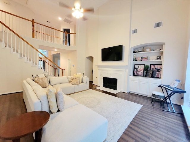 living room featuring dark wood-type flooring, built in features, ceiling fan, a high end fireplace, and a high ceiling