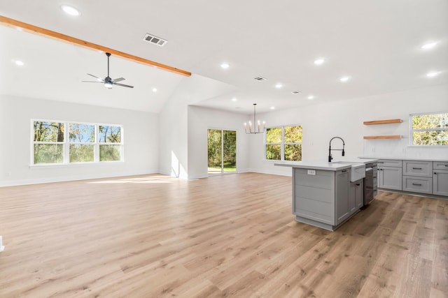 kitchen featuring gray cabinetry, vaulted ceiling with beams, decorative light fixtures, a kitchen island with sink, and light hardwood / wood-style floors