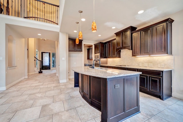 kitchen featuring appliances with stainless steel finishes, decorative light fixtures, an island with sink, sink, and light stone countertops