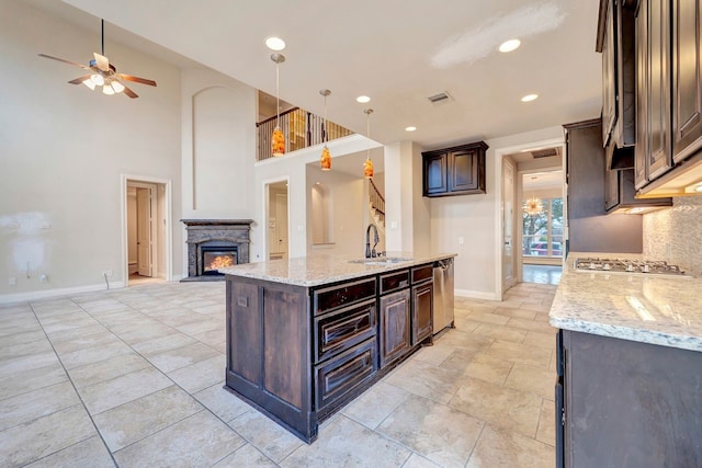 kitchen featuring pendant lighting, sink, a kitchen island with sink, dark brown cabinets, and light stone countertops