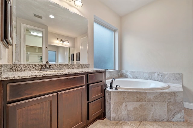 bathroom with tiled tub, vanity, and a healthy amount of sunlight