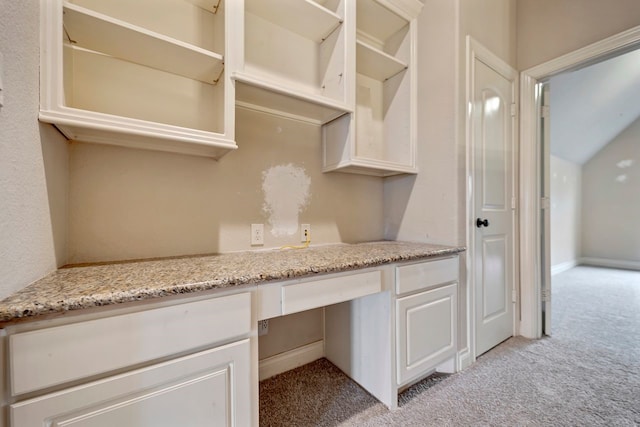 kitchen with white cabinetry, light stone countertops, built in desk, and light colored carpet