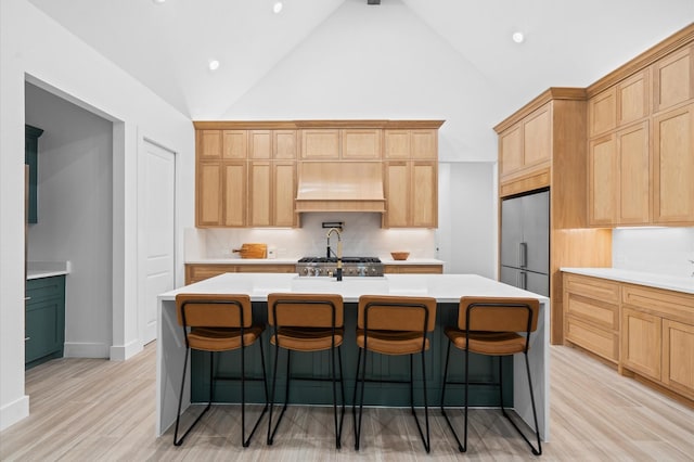 kitchen with beamed ceiling, a kitchen breakfast bar, a kitchen island with sink, custom range hood, and light wood-type flooring