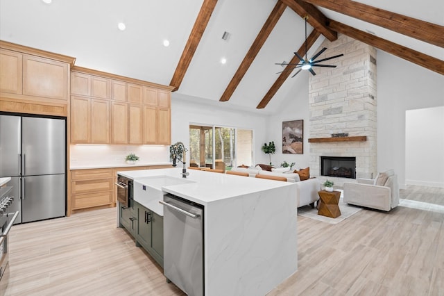 kitchen featuring appliances with stainless steel finishes, high vaulted ceiling, light brown cabinetry, a center island with sink, and beam ceiling