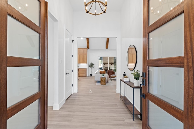 corridor featuring beam ceiling, light hardwood / wood-style flooring, and a chandelier