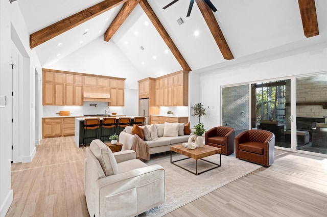 living room featuring beam ceiling, light wood-type flooring, sink, and high vaulted ceiling